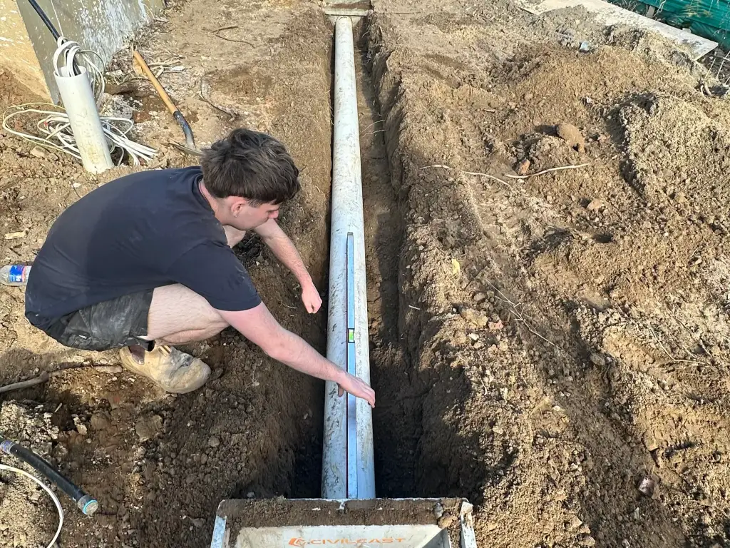 High-pressure jetter hose reel feeding into an open sewer inspection point on a back lawn
