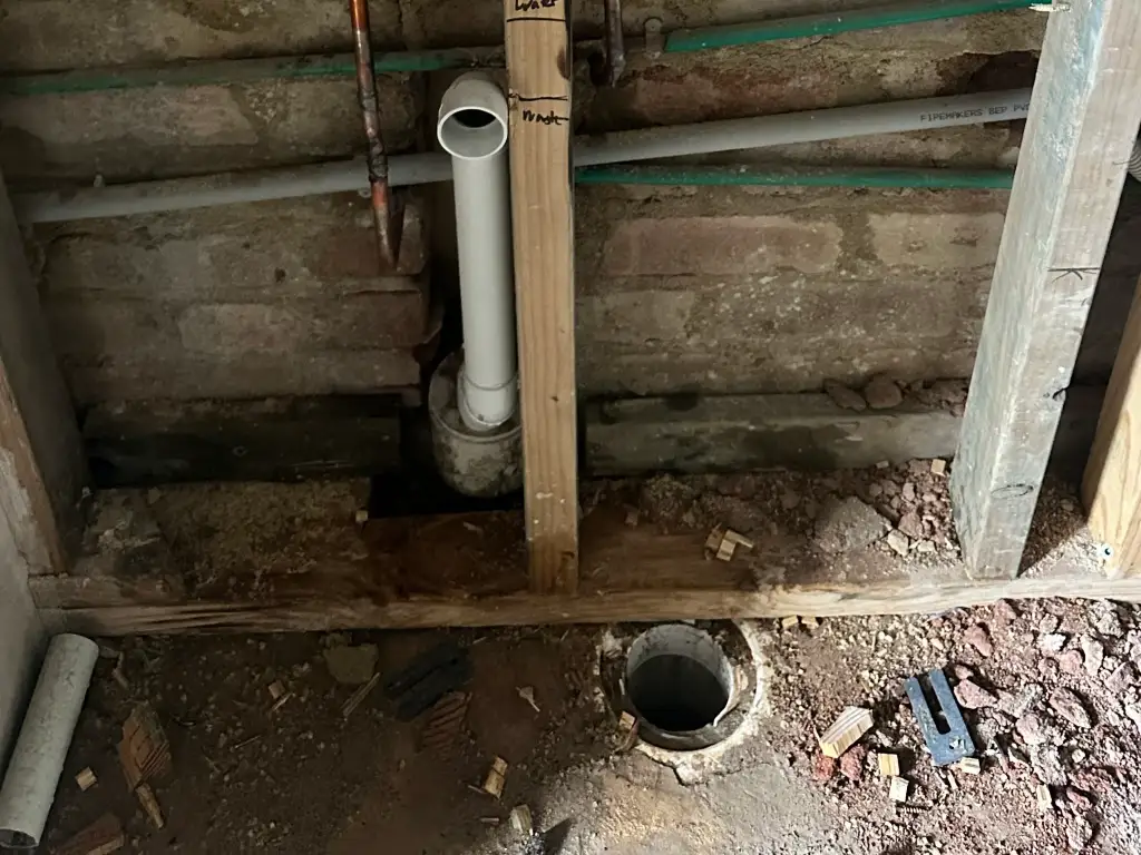 Burst copper water pipe exposed inside a brick wall cavity during an emergency repair